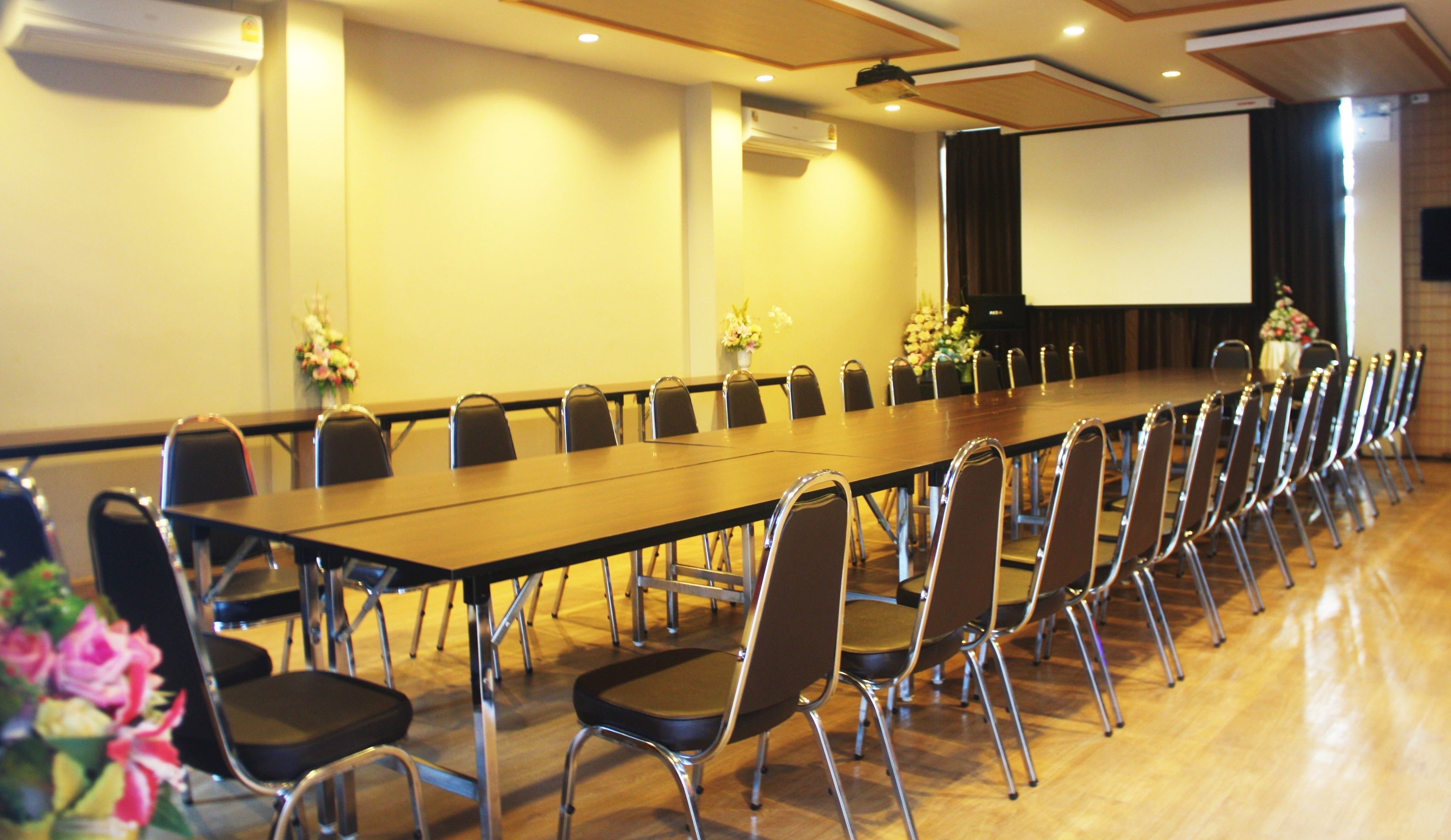 Une salle de conférence équipée d’une longue table, de chaises, d’un écran de projection et de climatiseurs.
