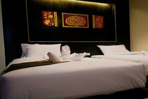 Quarto de hotel com duas camas, roupa de cama branca e cabeceira escura.