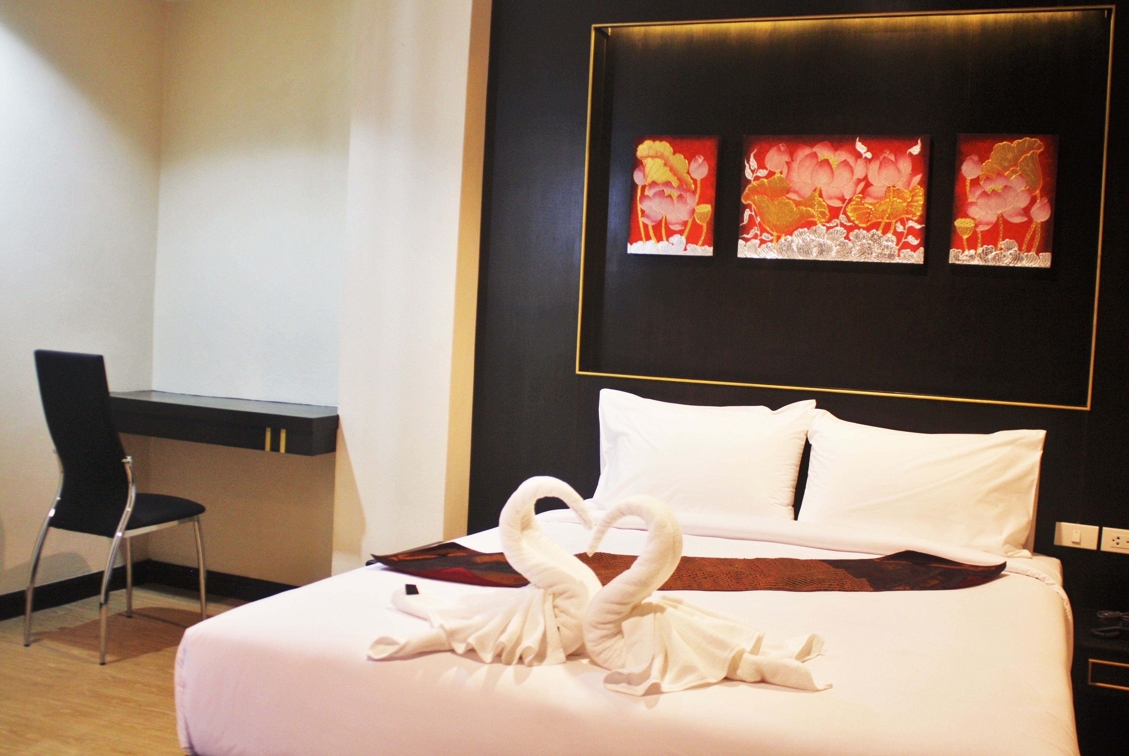A hotel room with a bed, a desk, and a chair. There are three paintings on the wall above the bed.