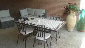 Une terrasse extérieure avec une table et des chaises, un canapé et un grand vase rempli de fleurs.