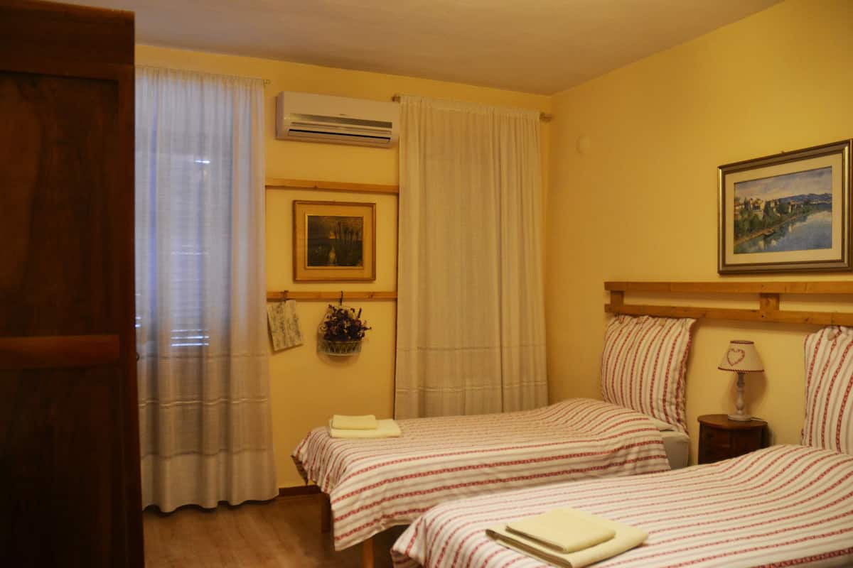 Habitación de hotel con dos camas, una mesita de noche con lámpara, un cuadro enmarcado en la pared y un equipo de aire acondicionado.