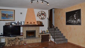 Un salon avec une cheminée, un téléviseur, une bibliothèque et un escalier.