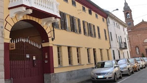 Un bâtiment jaune avec un balcon rouge et blanc, une tour de l’horloge et des voitures garées devant.
