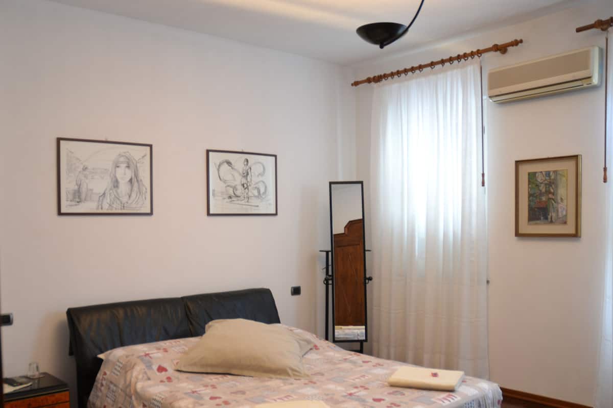Un dormitorio con cama, mesita de noche, espejo y cuadros en las paredes.