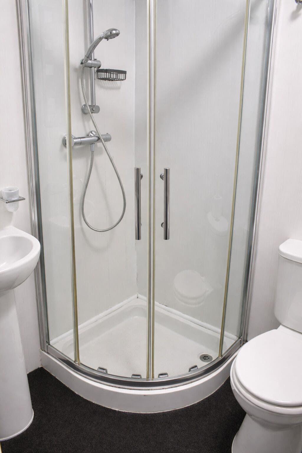 A corner shower enclosure with a glass door, a handheld showerhead, and a handheld shower attachment.