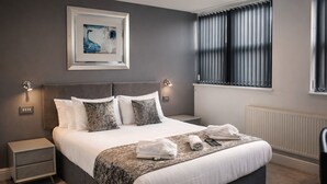 A neatly made bed with a patterned bedspread, a bedside table with a lamp, and a window with blinds.