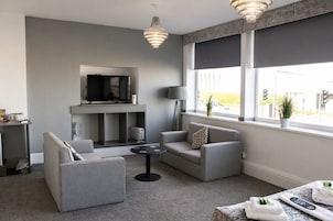 Een moderne woonkamer met grijze banken, een flatscreen televisie, een open haard en grote ramen met uitzicht.