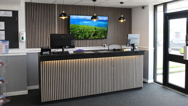 A reception desk with a flat-screen TV, two pendant lights, and a view of greenery outside.
