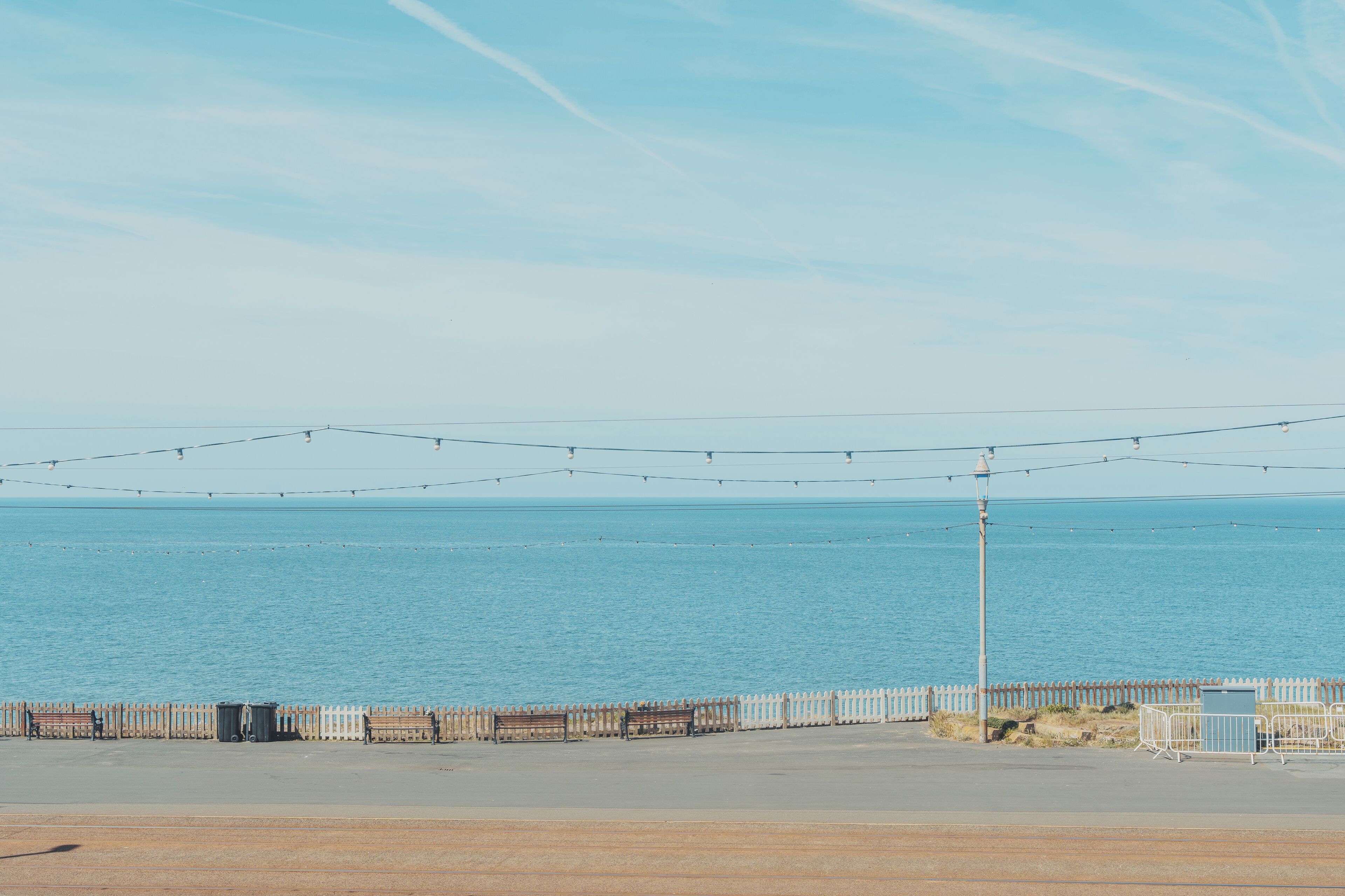 A coastal promenade with a white fence, benches, and string lights.