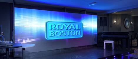 A stage with a neon sign reading "ROYAL BOSTON" and a piano on the right.