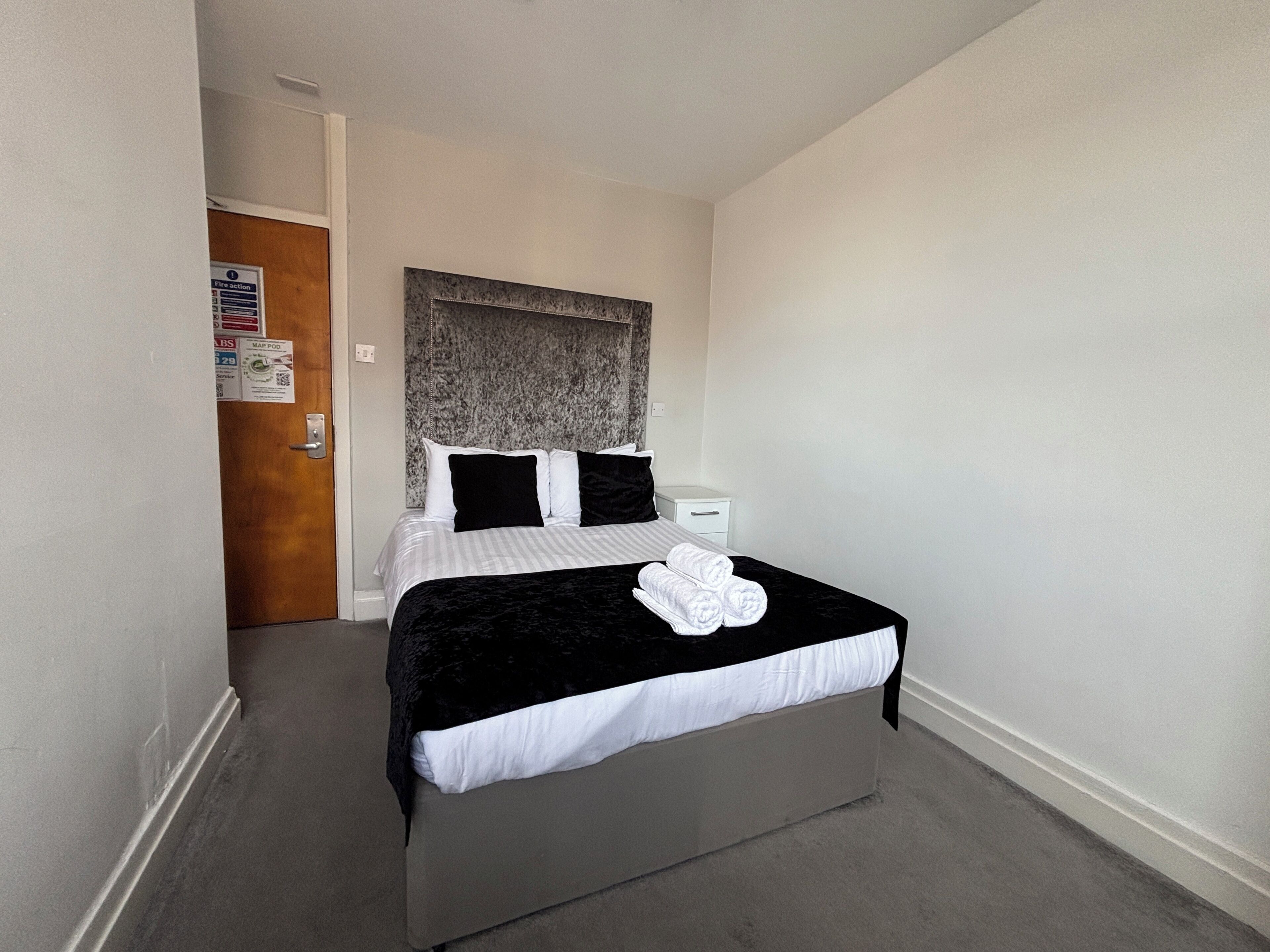 A hotel room with a bed, a nightstand, a door, and a wall with a fire action poster.