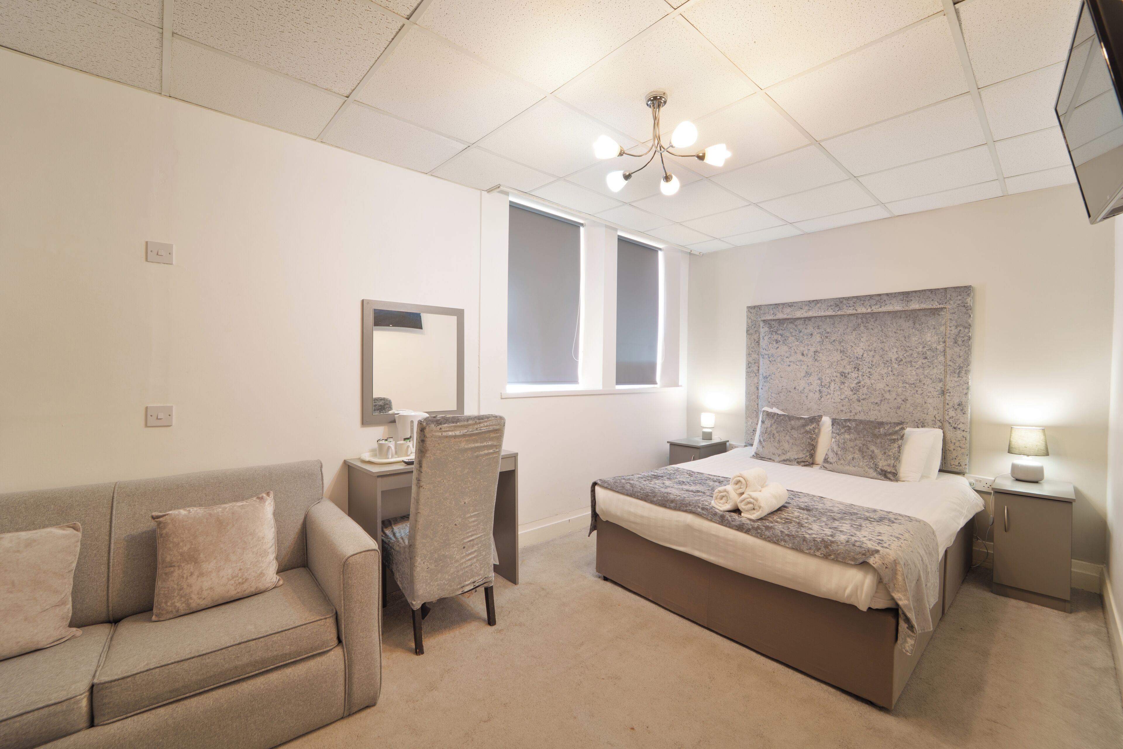 A hotel room with a bed, a desk, a chair, a small cabinet, and a television.