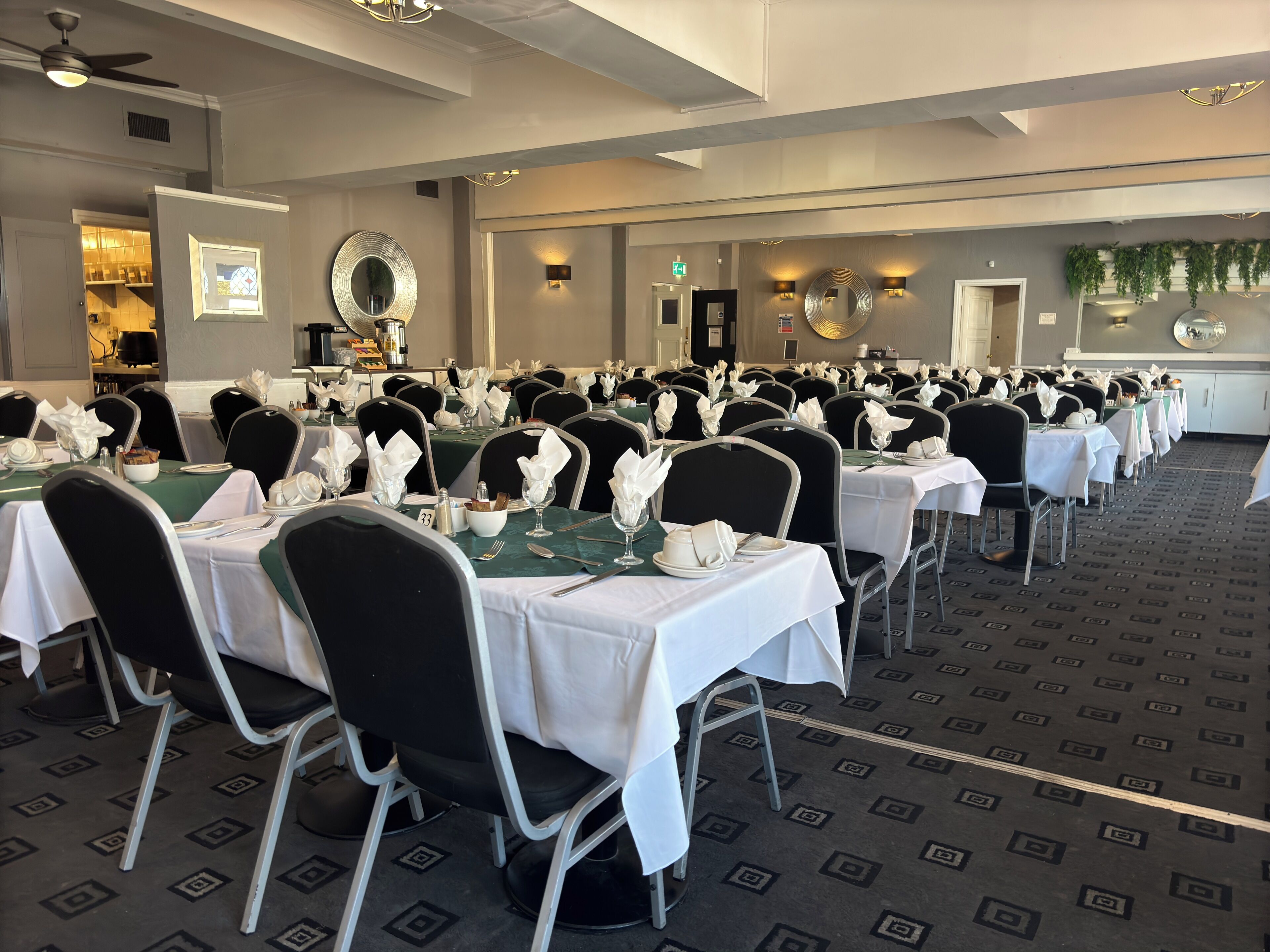 A banquet hall with rows of tables set for a formal event, featuring white tablecloths, black chairs, and floral centerpieces.