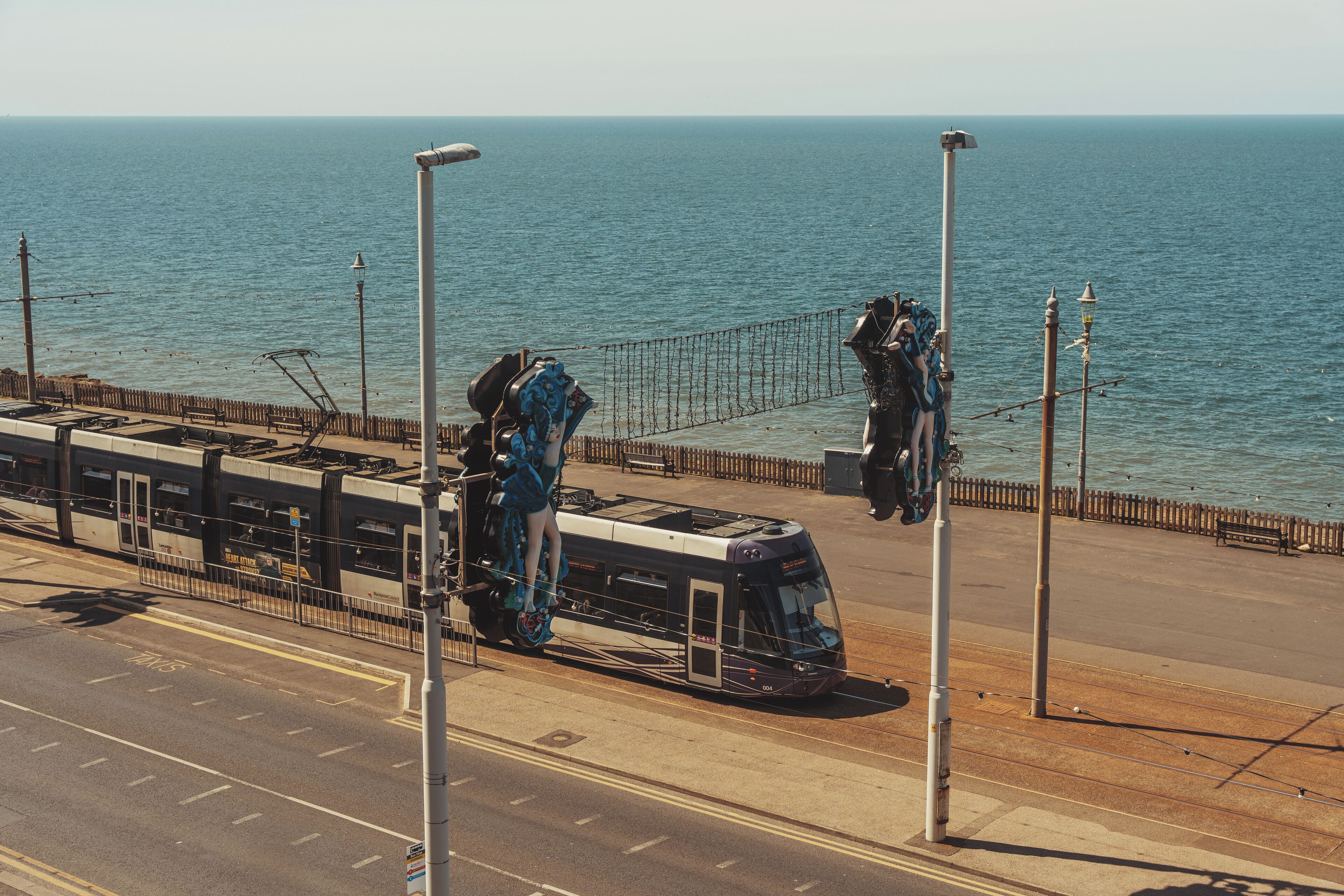 A tram with passengers, a coastal walkway, and the sea in the background.