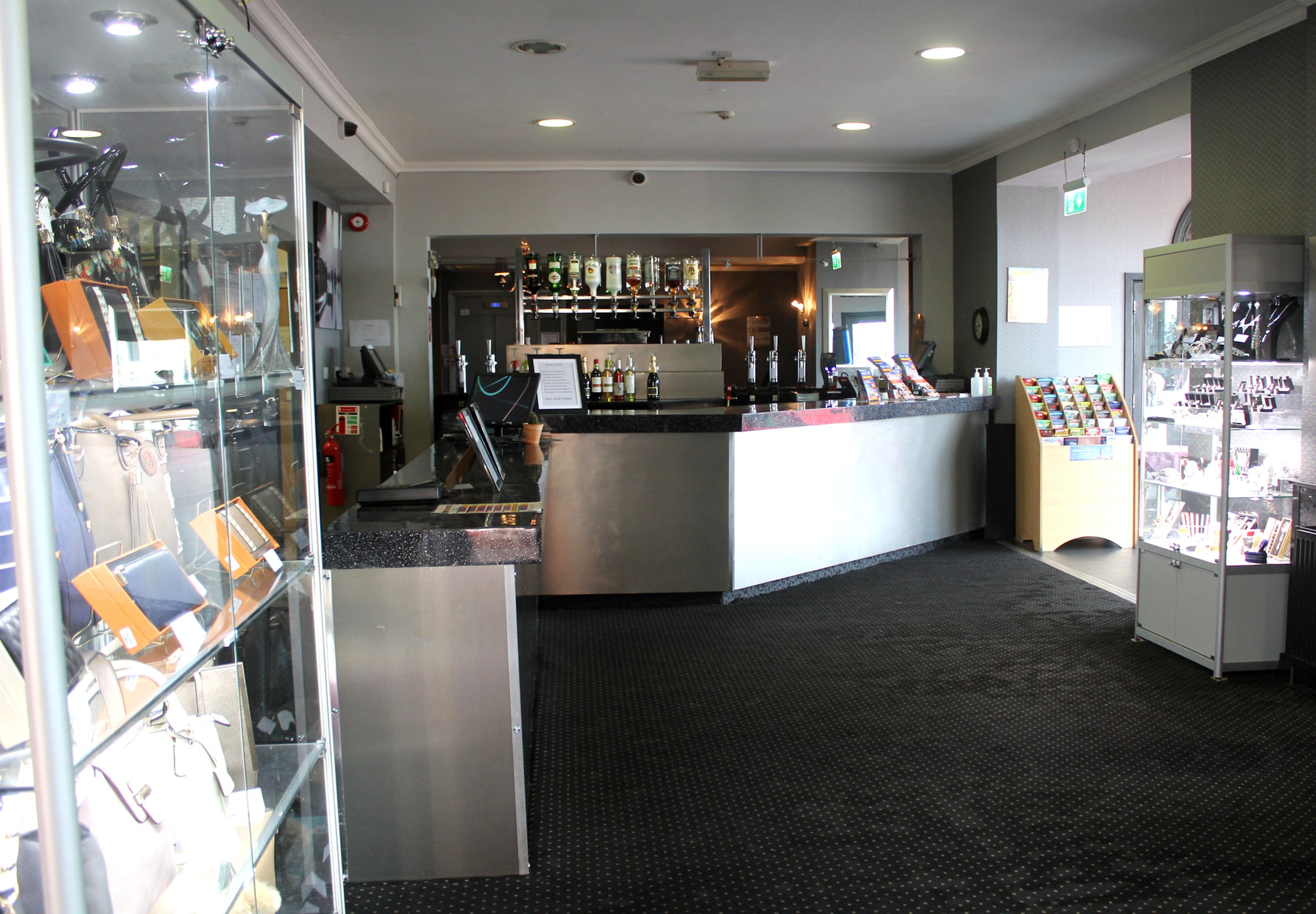 A hotel lobby with a reception desk, a glass display case with luggage, a bar area, and a shoe display.
