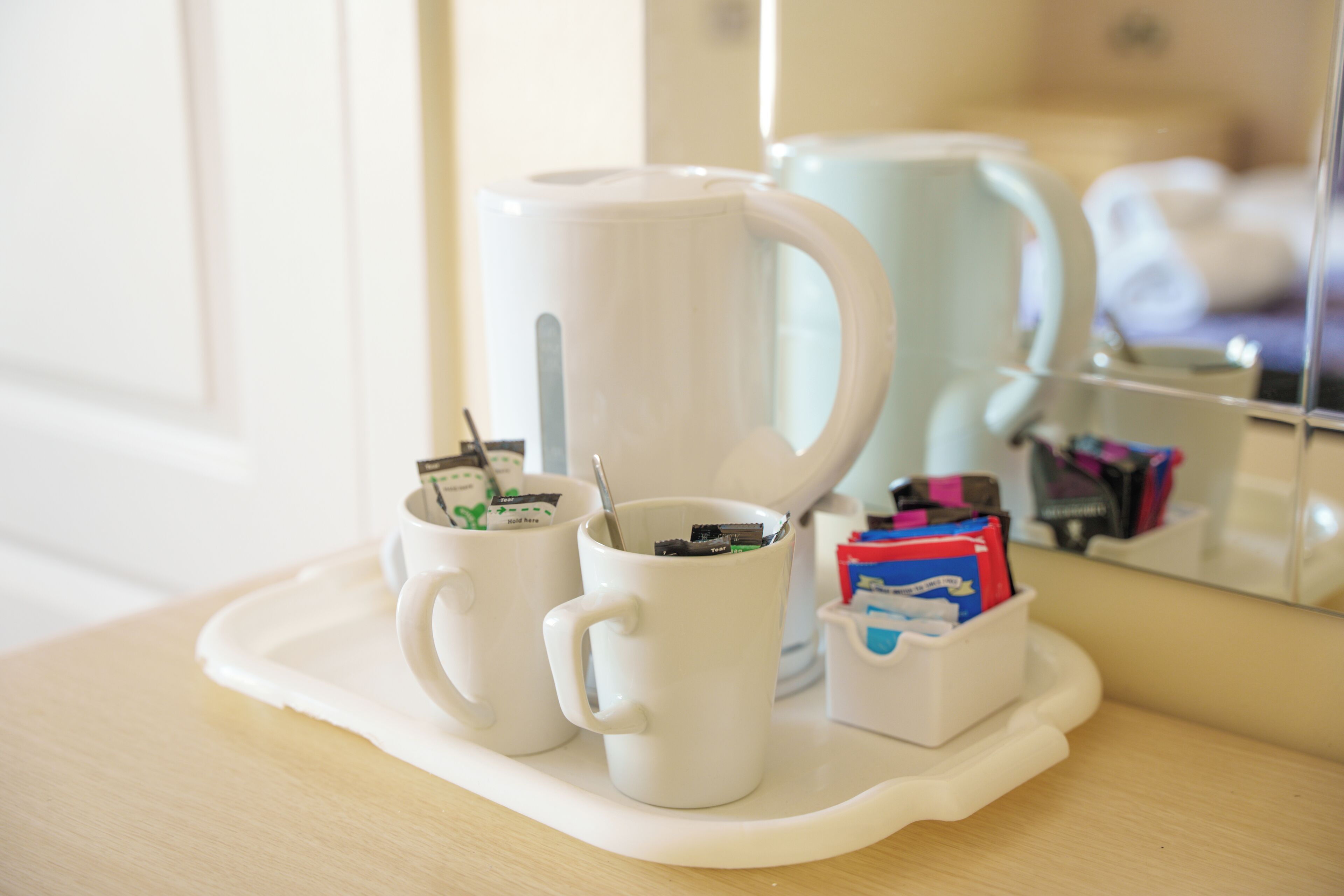 A tray with two white mugs, one with a spoon and a packet, and a small container with colorful items.