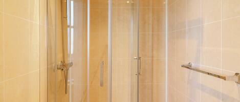 A glass-enclosed shower with a white bathtub and a towel rack.