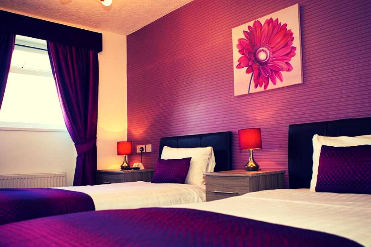Habitació d'hotel amb dos llits, un quadre gran de flors a la paret i una finestra amb cortines.