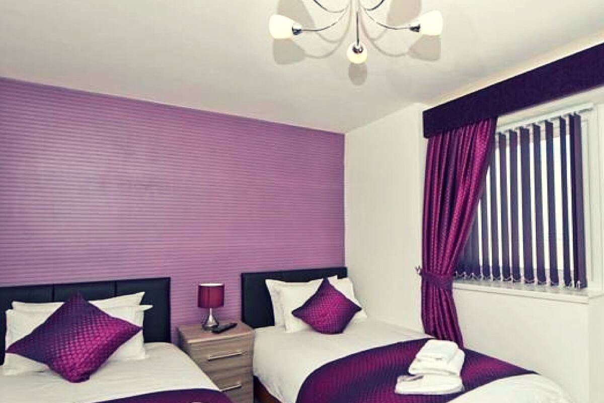 Una habitació d'hotel amb dos llits, una tauleta de nit amb una làmpada i una finestra amb cortines.