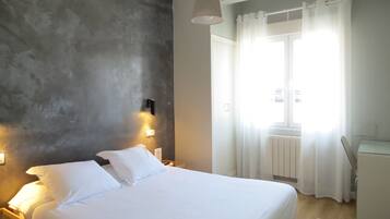 Relax in a spacious room with a large bed, wall-mounted lights, and a window with sheer curtains.