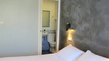 Ein Hotelzimmer mit einem Bett, einem Nachttisch, einer Wandleuchte und Blick ins Bad.