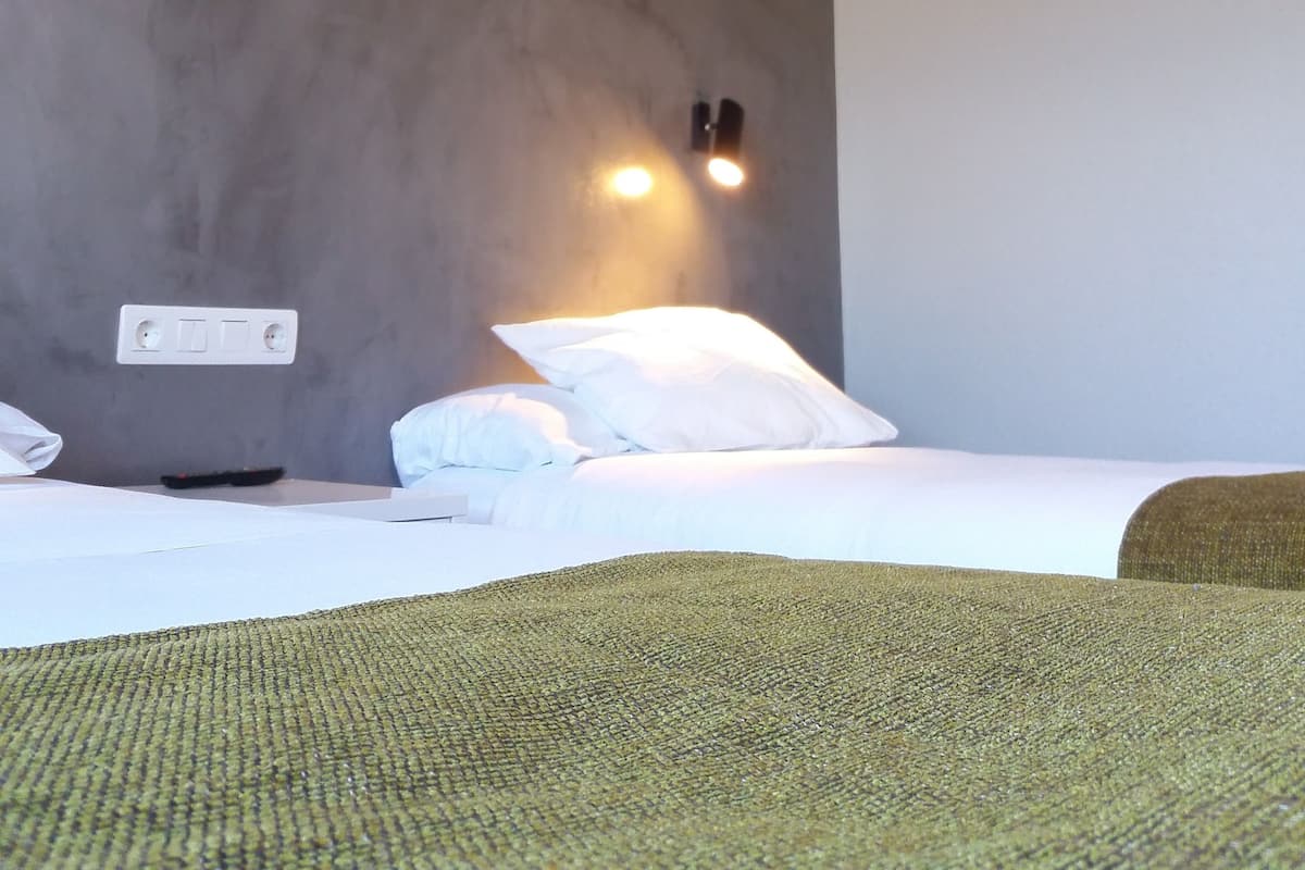 Habitación de hotel con cama, una manta verde, una lámpara de pared y un enchufe.