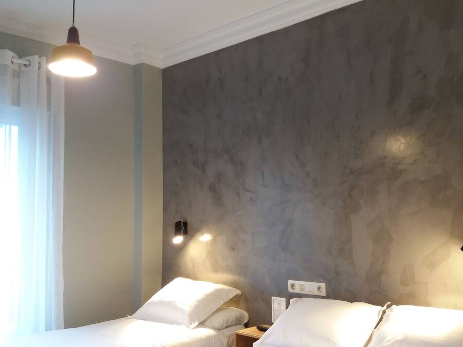 Habitación de hotel con dos camas, una lámpara en el techo y una pared con textura.
