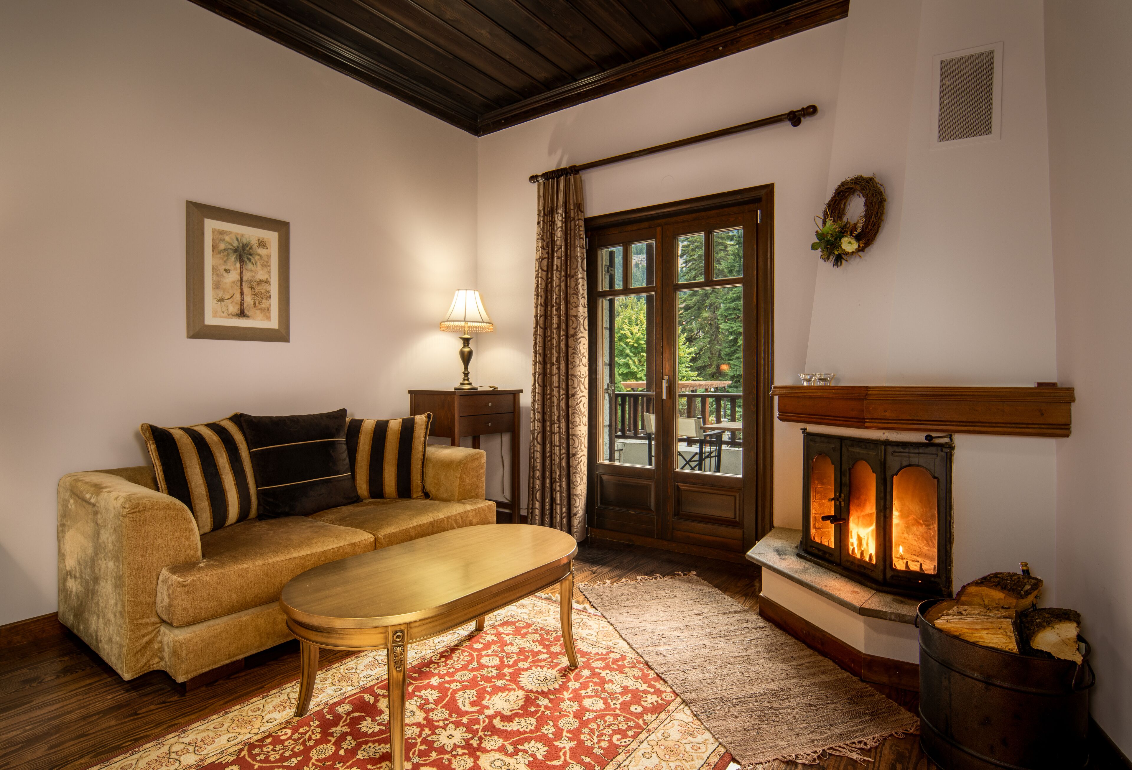 A cozy living room with a sofa, a wooden coffee table, a fireplace, and a view through a glass door.