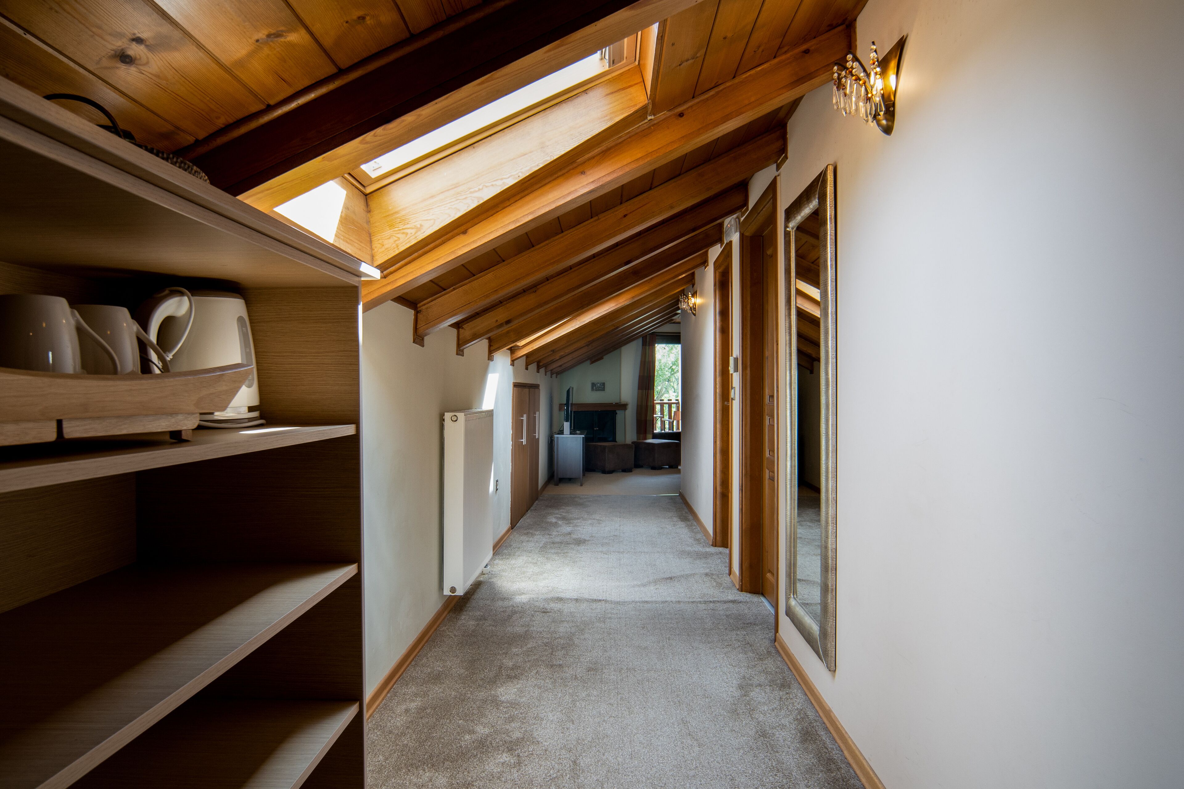 A narrow hallway with wooden beams and a skylight, leading to a kitchen area.