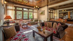 A spacious living room with a large window, wooden ceiling, and a cozy seating area with a sofa and chairs. - Giamandes Hotel (Pyli)