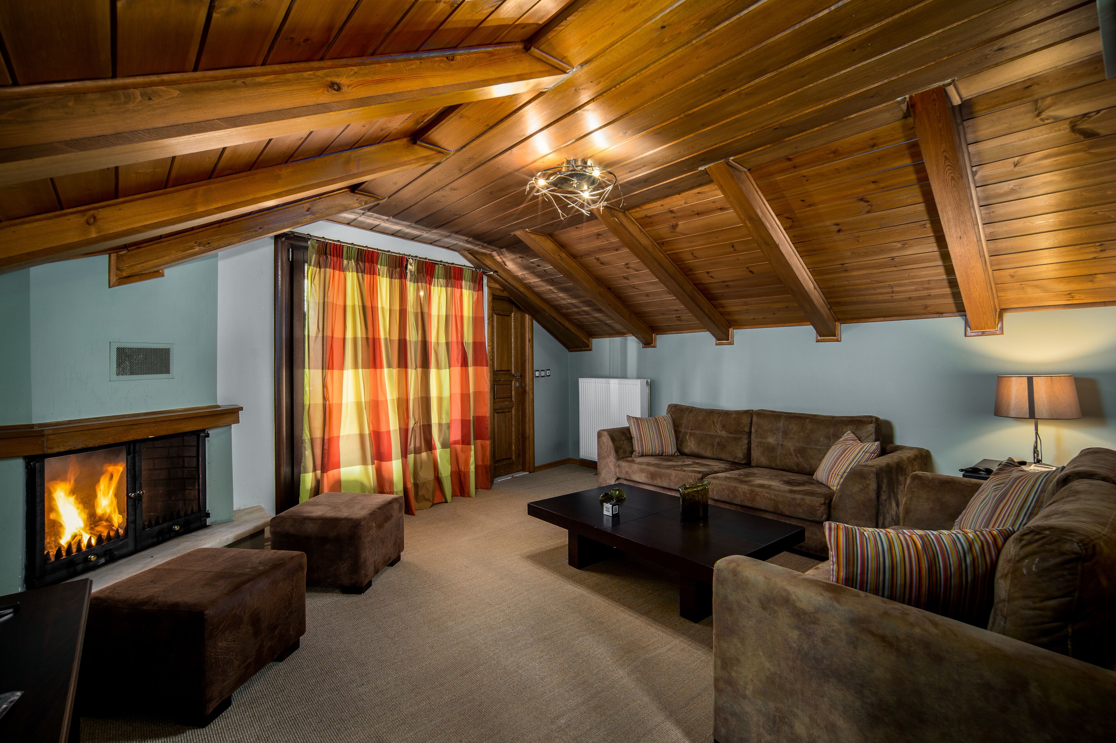 Una sala acogedora con chimenea, vigas de madera en el techo, un conjunto de sofás y una cortina a rayas.