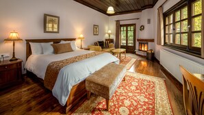 A bedroom with a large bed, bedside lamps, a bench, a small table, and a fireplace. - Giamandes Hotel (Pyli)