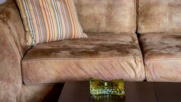 A brown leather sofa with a striped pillow and a glass vase on a wooden table. Two abstract paintings are hung on the wall above the sofa.