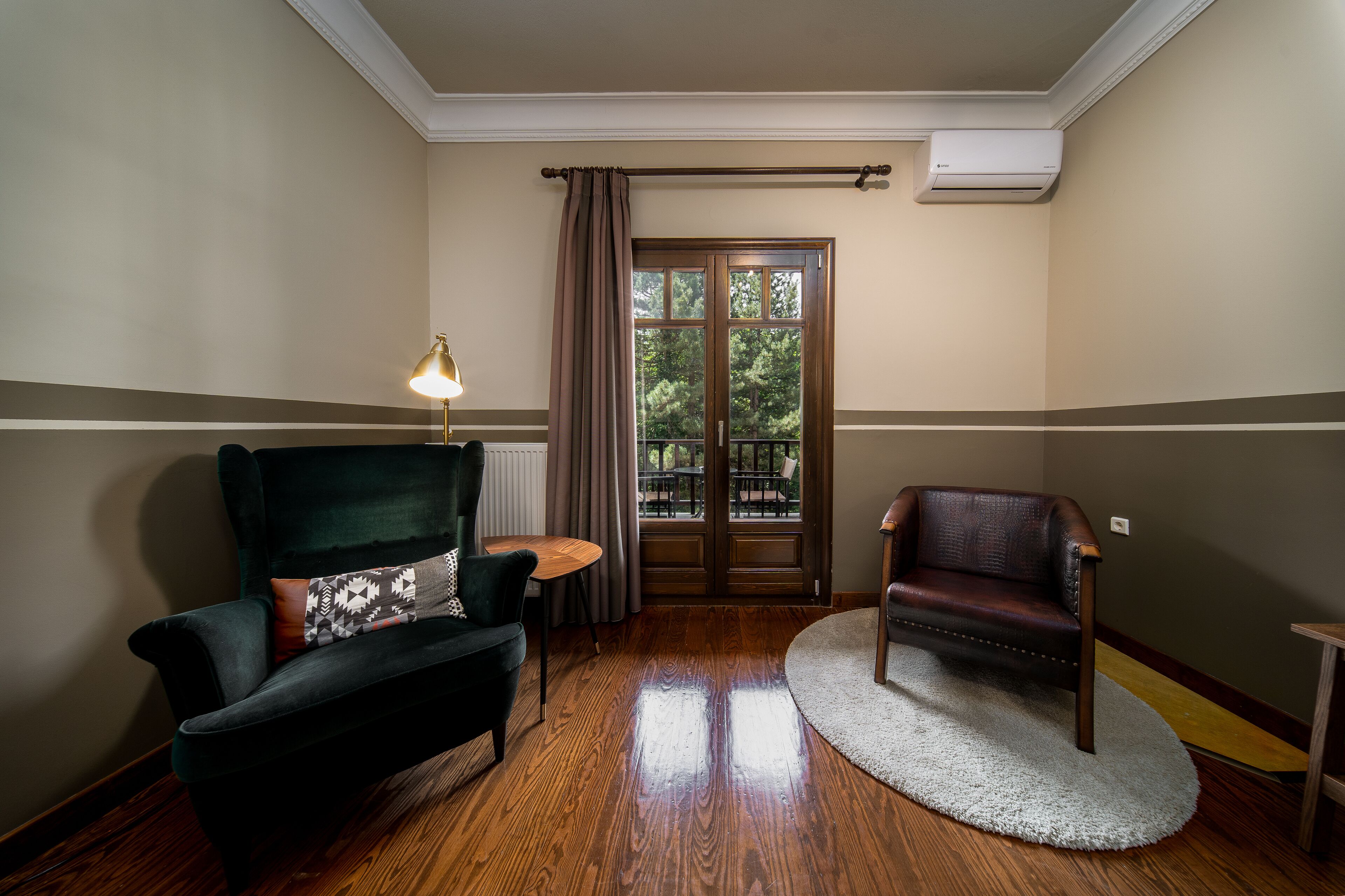 Una habitación con un sillón verde oscuro, un sillón de cuero marrón, una mesita redonda y una alfombra blanca.