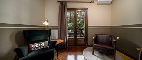 Una habitación con un sillón verde oscuro, un sillón de cuero marrón, una mesita redonda y una alfombra blanca.