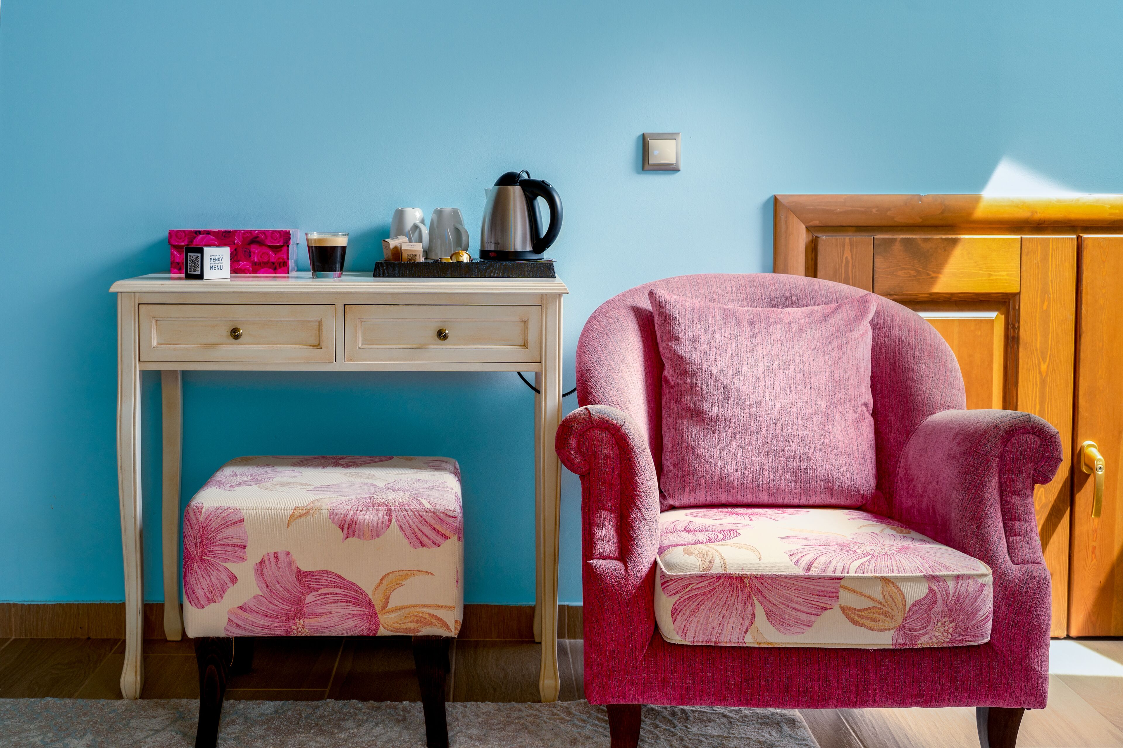 A room with a wooden desk, a pink armchair, and a matching ottoman.