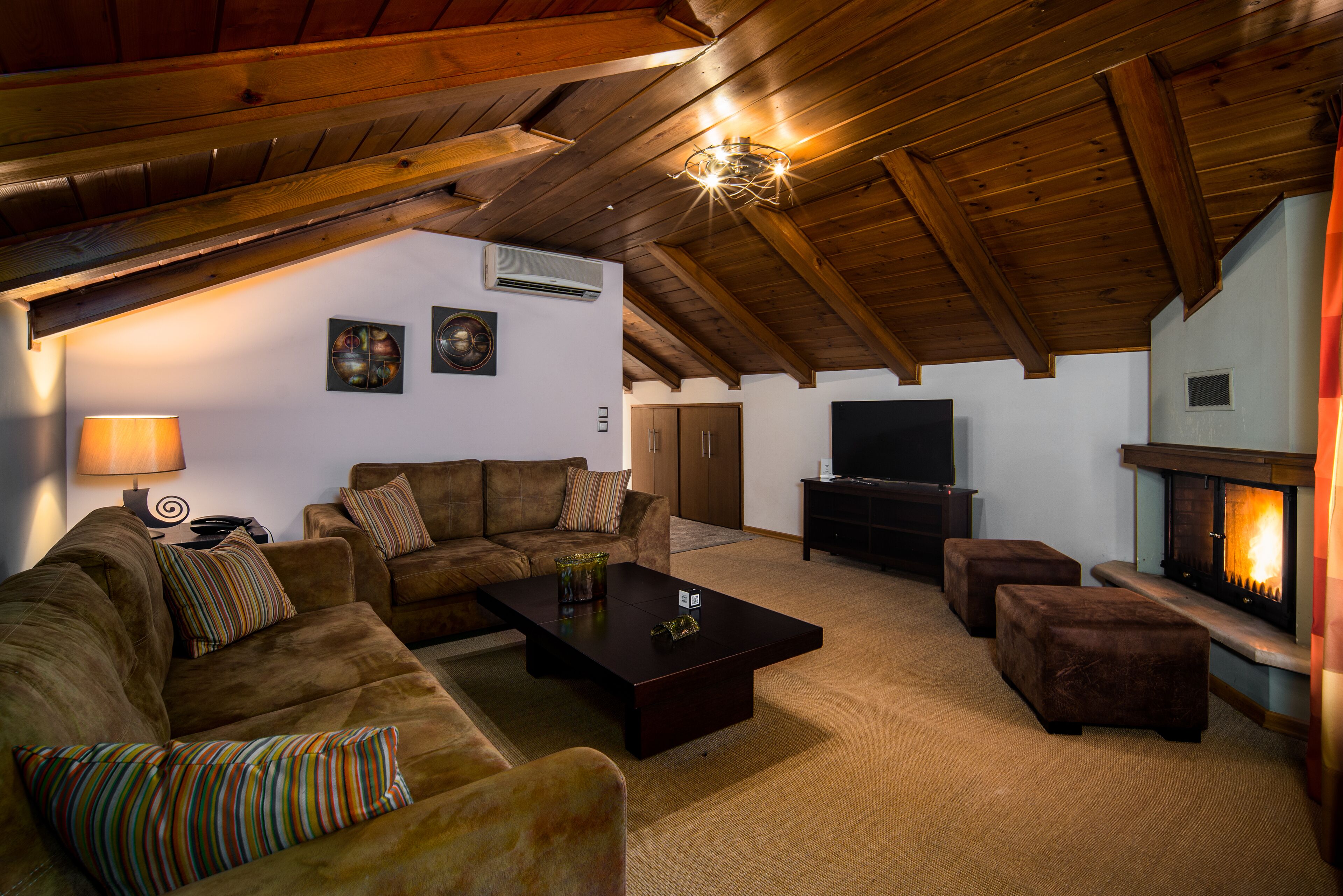A cozy living room with a fireplace, wooden ceiling beams, and a flat-screen TV.