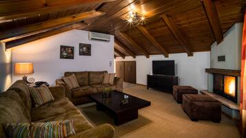 A cozy living room with a fireplace, wooden ceiling beams, and a flat-screen TV.