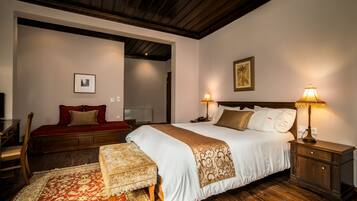 A bedroom with a large bed, two bedside lamps, a wooden nightstand, a red sofa, and a patterned rug.