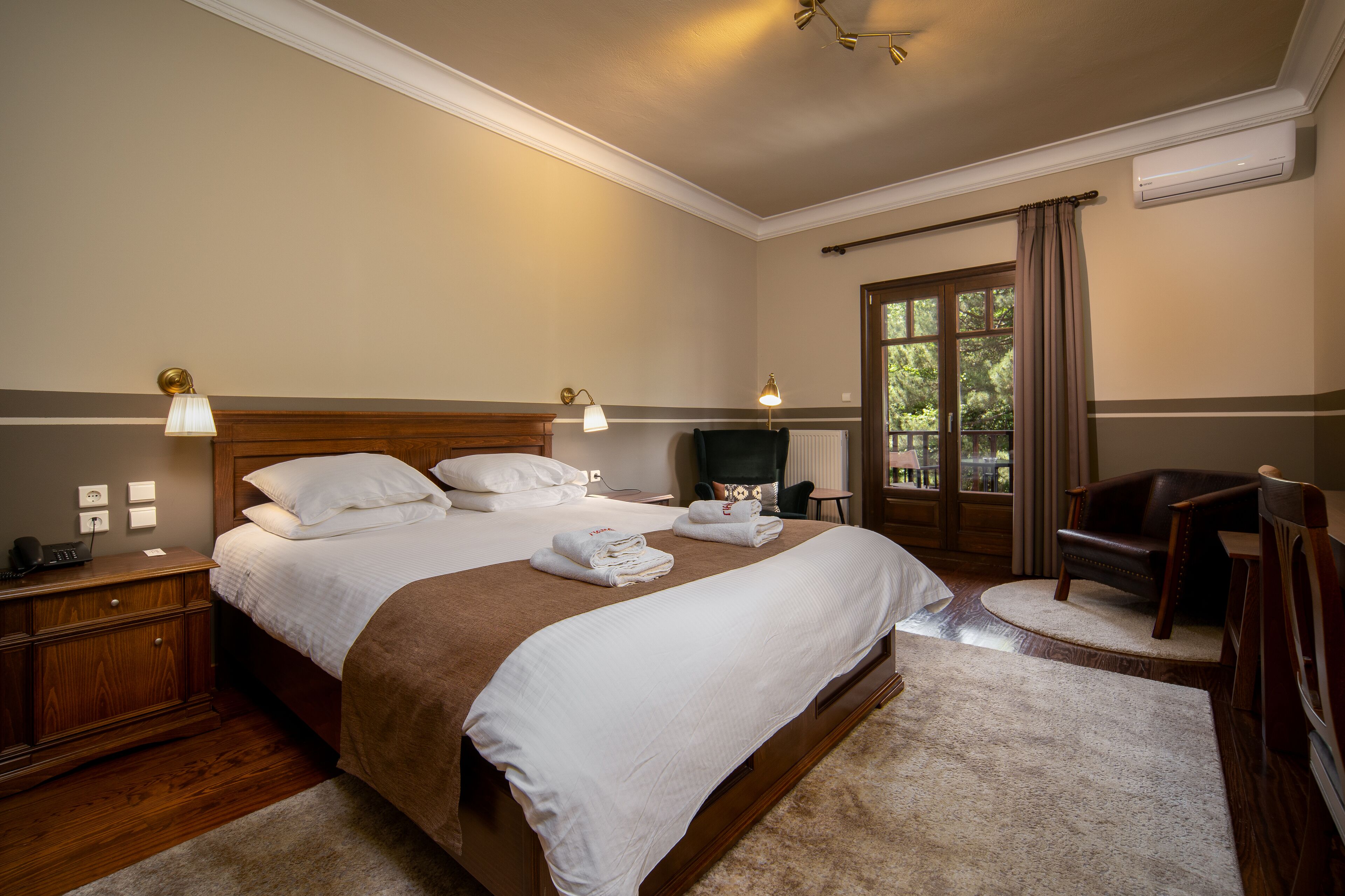 A neatly arranged bedroom with a large bed, bedside lamps, a chair, and a view of the outdoors through a window.