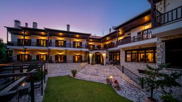 A multi-story building with a stone facade, multiple balconies, and a central courtyard with a lawn and seating area.