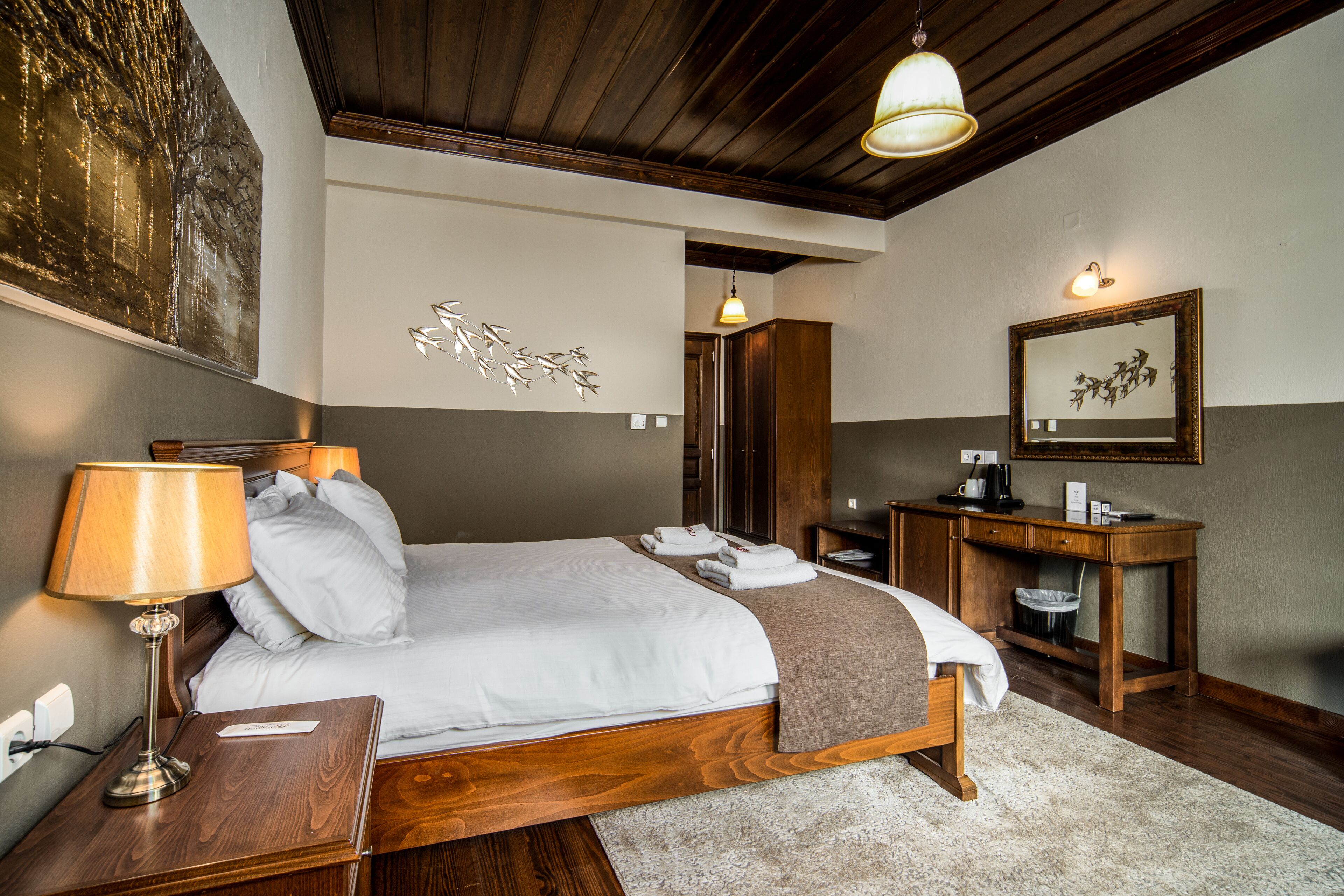 A hotel room with a wooden bed, a nightstand, a desk, and a mirror.
