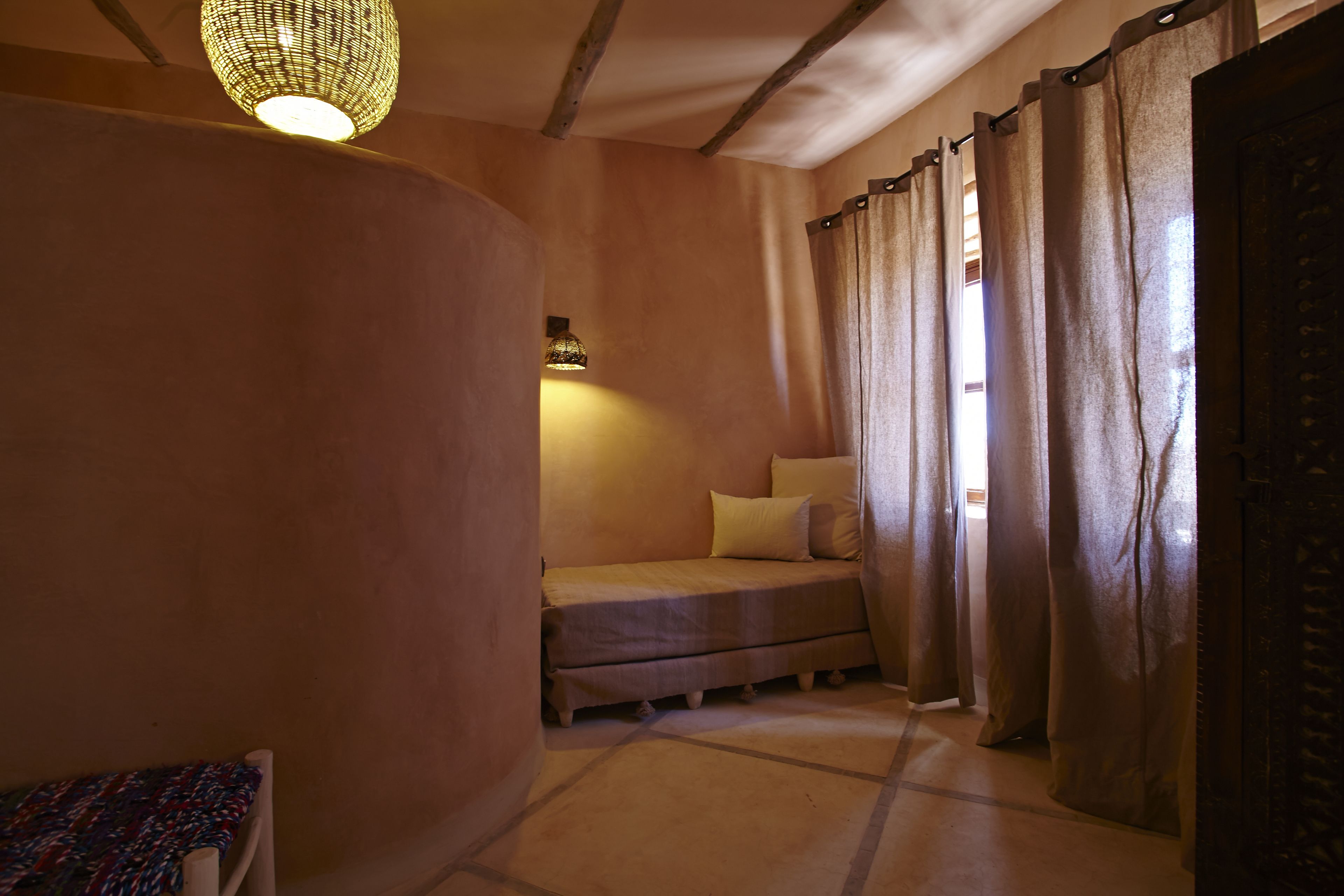 A cozy room with a bed, a hanging light fixture, and a window with curtains.