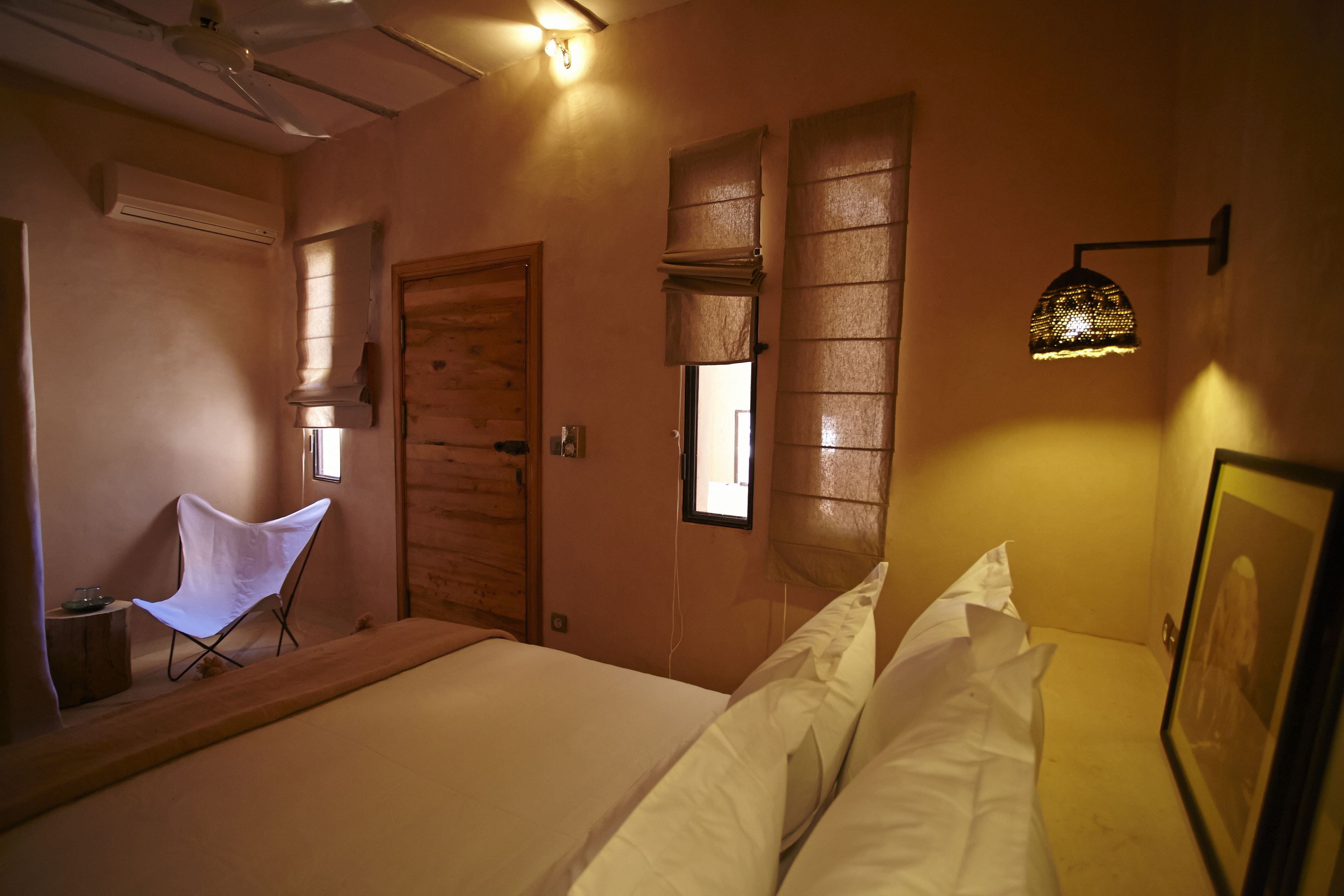 Quarto com cama, cadeira, janela e luminária na parede.