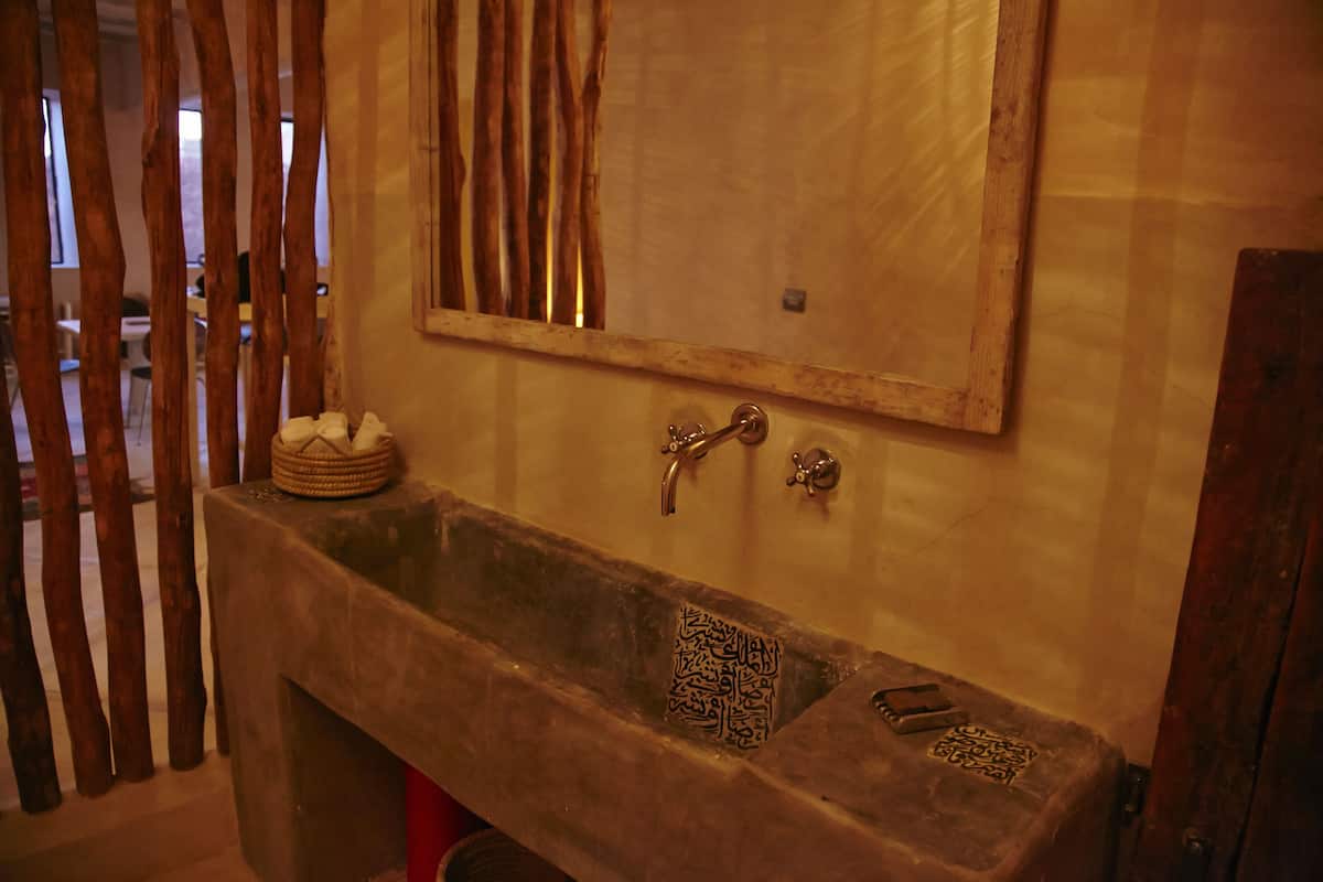 Eine Steine Badewanne mit Holzrahmen, ein Spiegel darüber und eine kleine Ablage mit einem gewebten Korb und einem dekorativen Gegenstand.