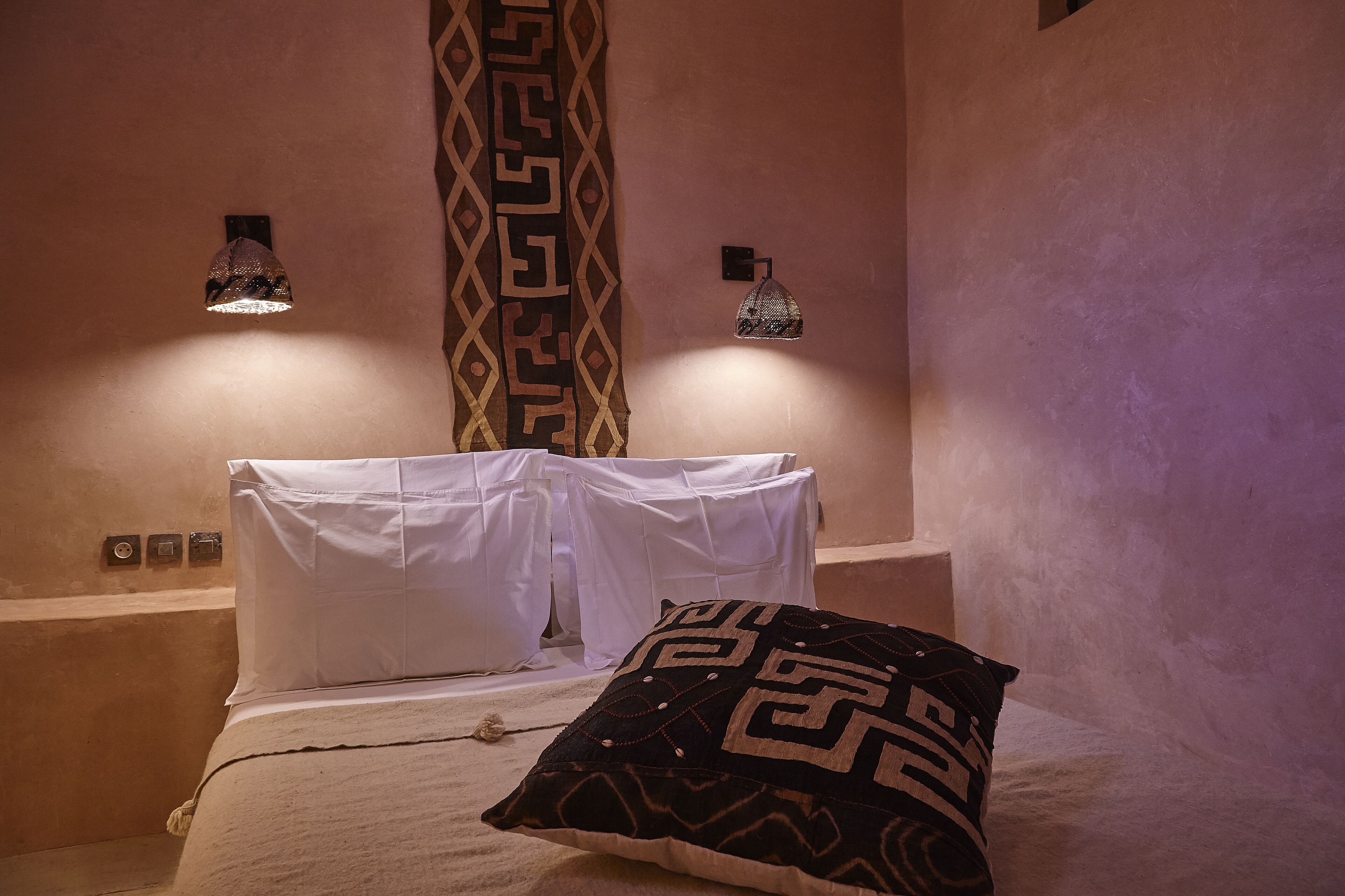 A bed with white linens, a patterned pillow, and two wall-mounted lamps.