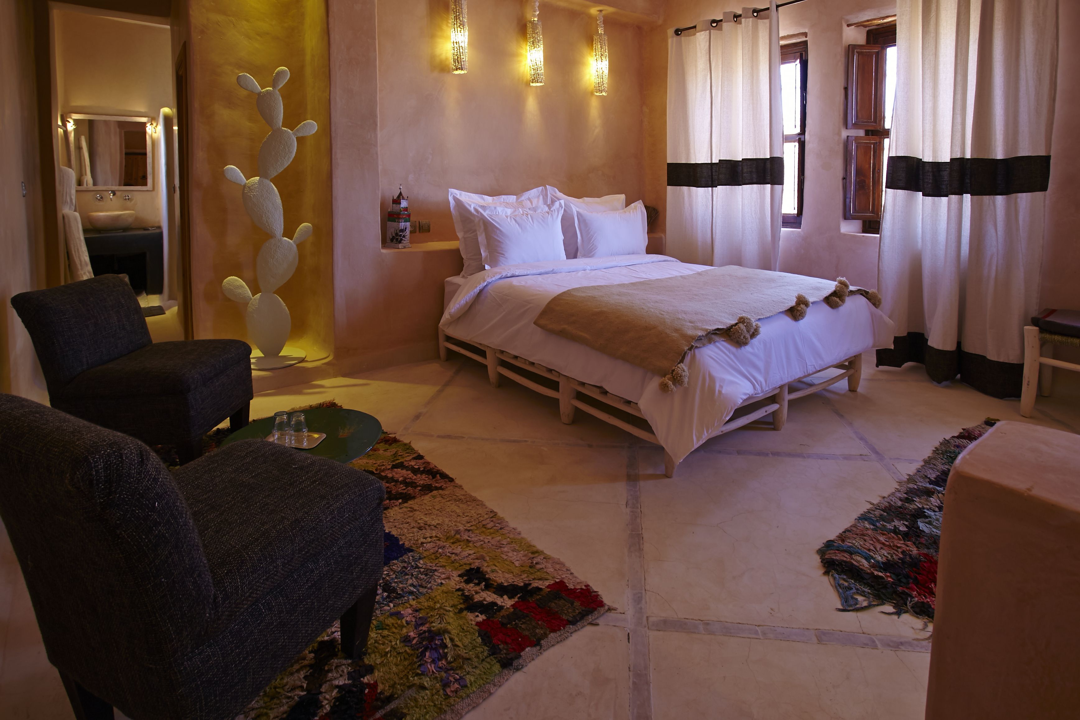 Une chambre à coucher comprenant un lit, une chaise, une petite table, un tapis et un élément décoratif mural.