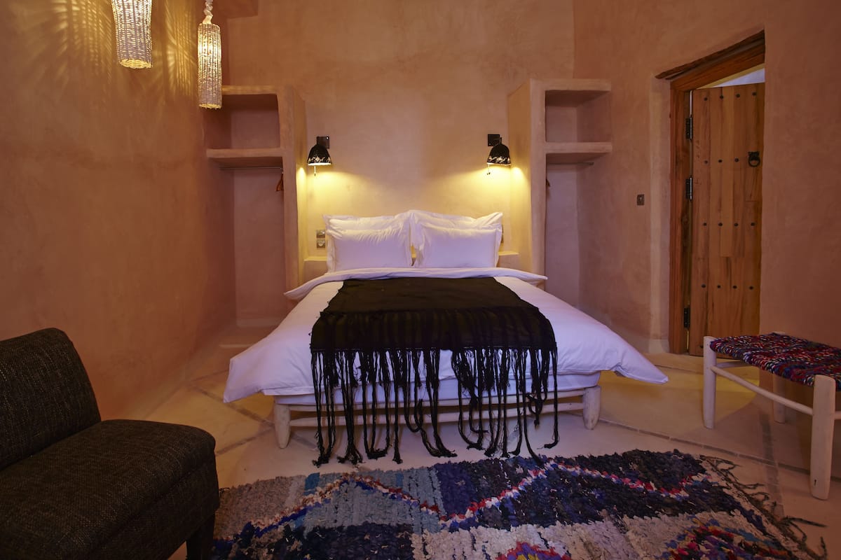 Ein Schlafzimmer mit Bett, Nachttischen, einem Sessel, einer Bank und einer Tür.