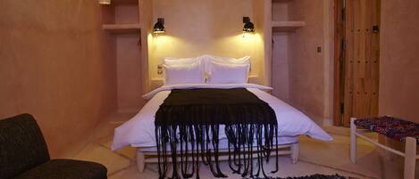 A bedroom with a bed, bedside tables, a chair, a bench, and a door.