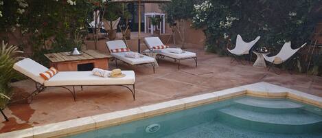 A pool area with lounge chairs, a small table, and a pergola with flowers.